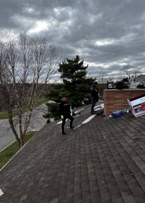 A man is standing on top of a roof with a tree in the background.