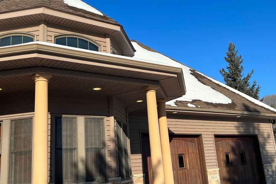A house with a porch and a garage with snow on the roof