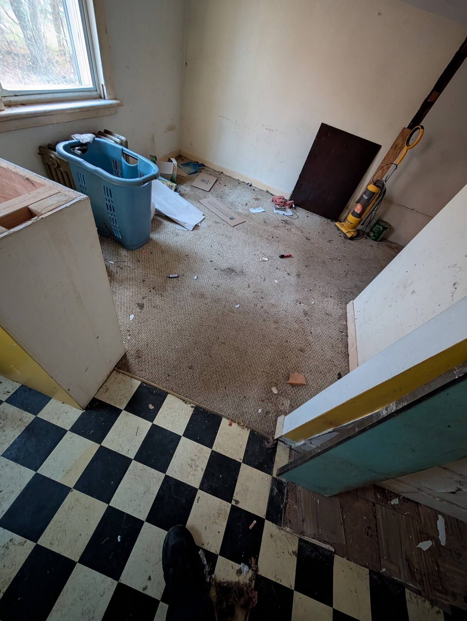 Black and white checkered floor leads to a small, cluttered room with a blue bathtub and debris.