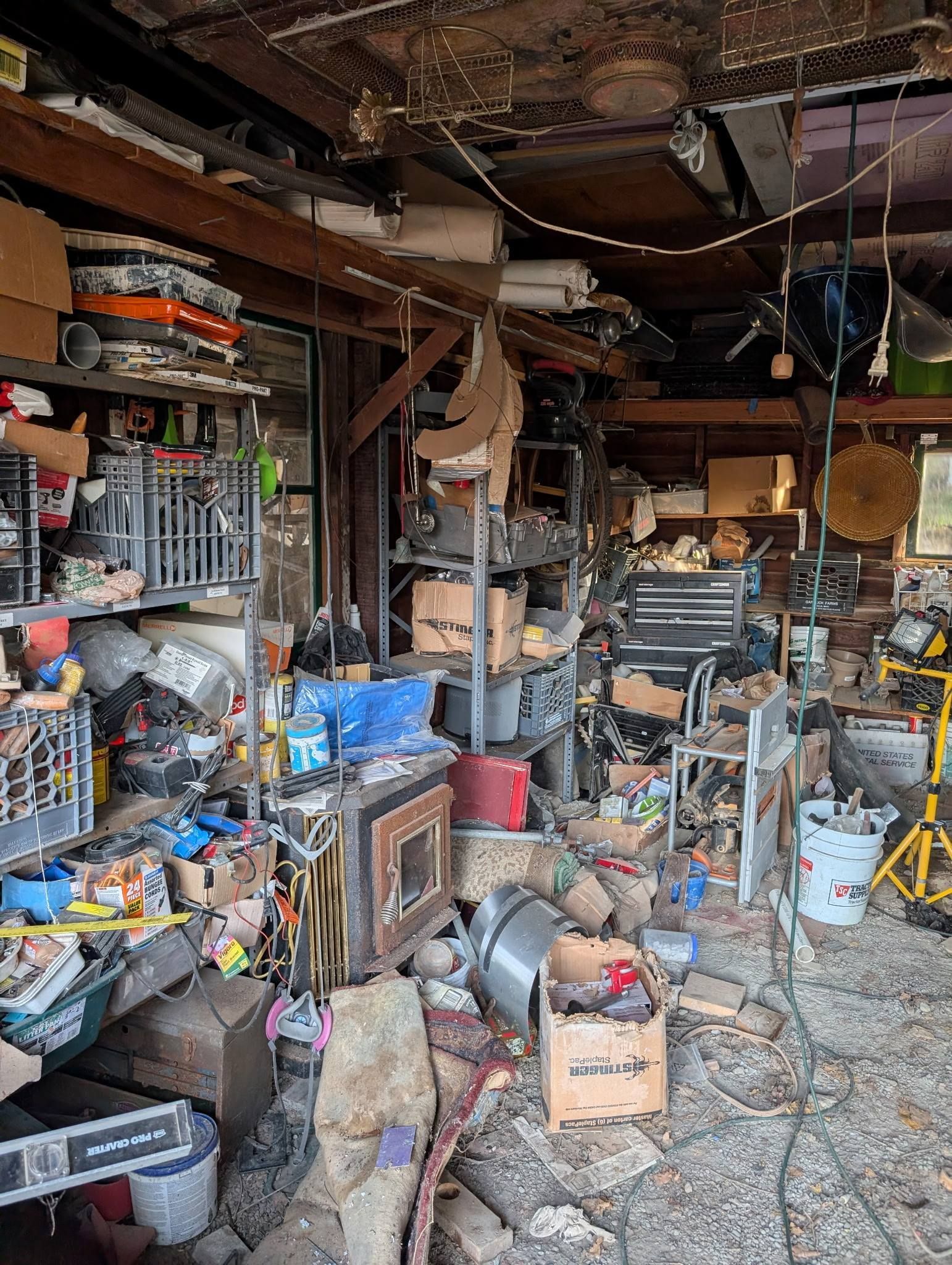 Cluttered garage interior filled with tools, boxes, and various items; shelves and work areas.