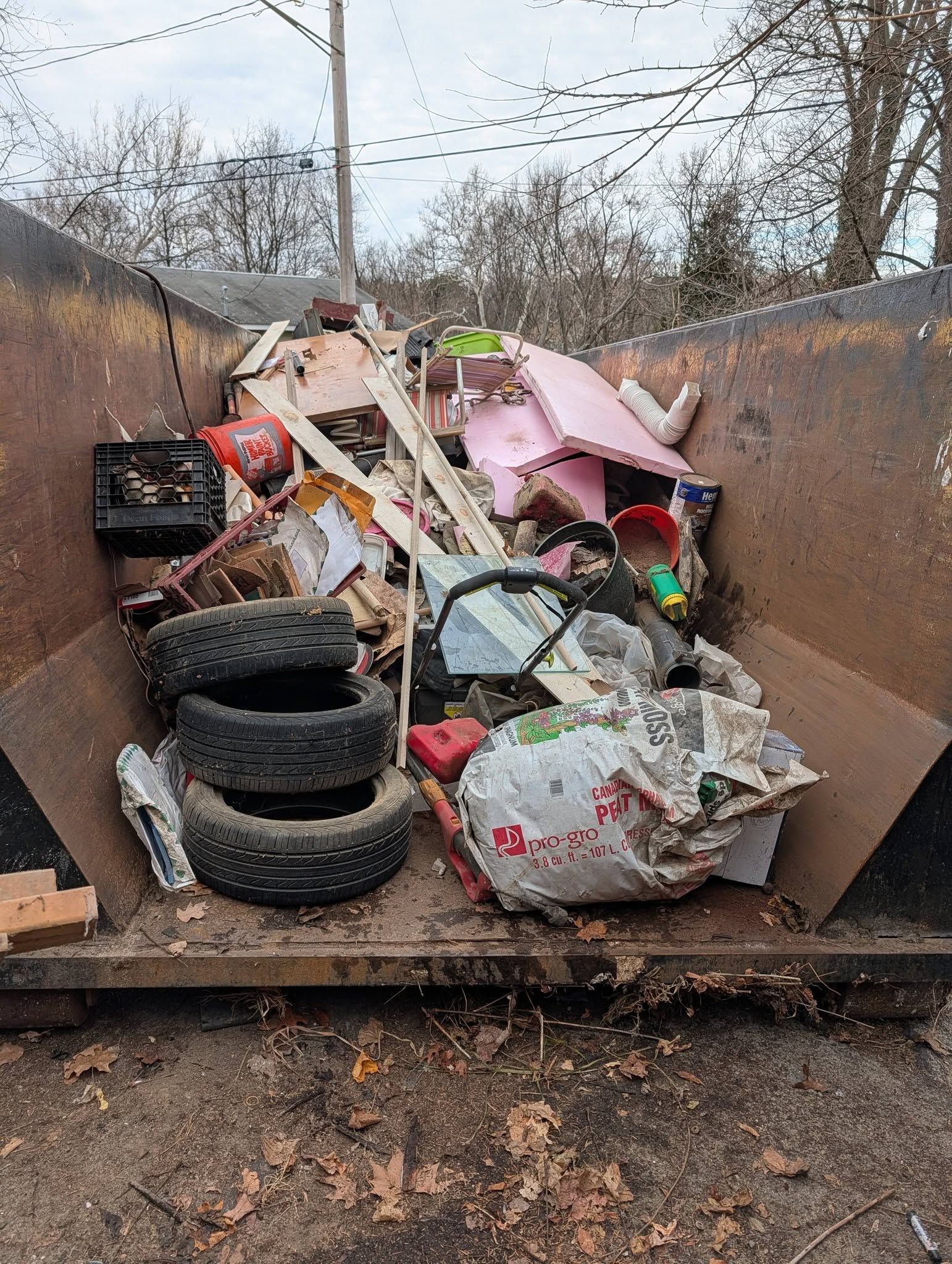 Dumpster filled with assorted debris including tires, wood, and pink plastic.