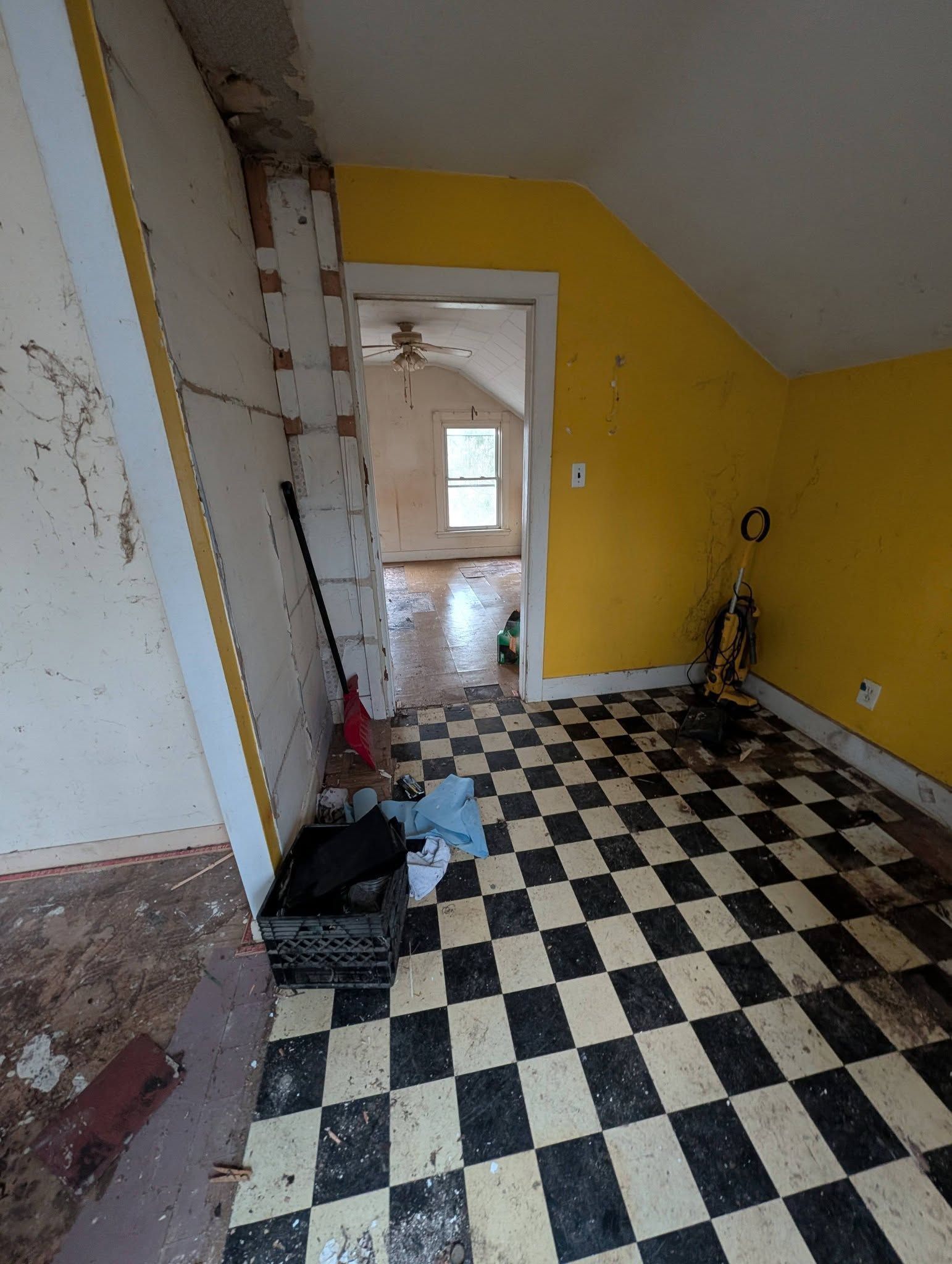 Room with checkered floor, yellow walls, doorway to another room, debris present.