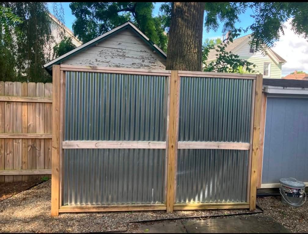 Two corrugated metal privacy screens with wood frames in a backyard.