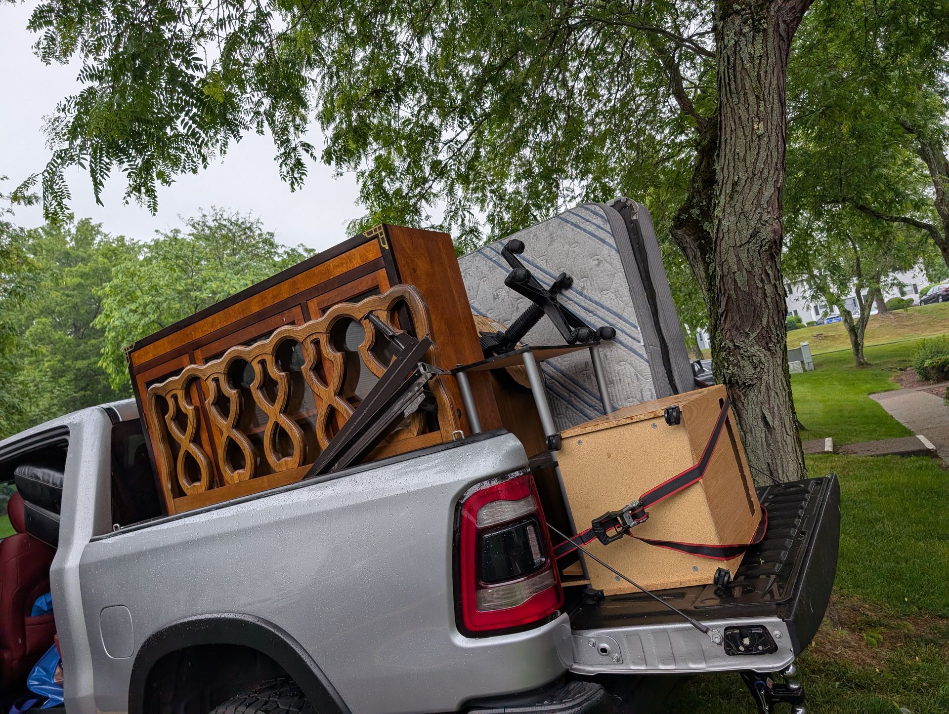 Pickup truck bed loaded with furniture and a mattress in a grassy outdoor setting.