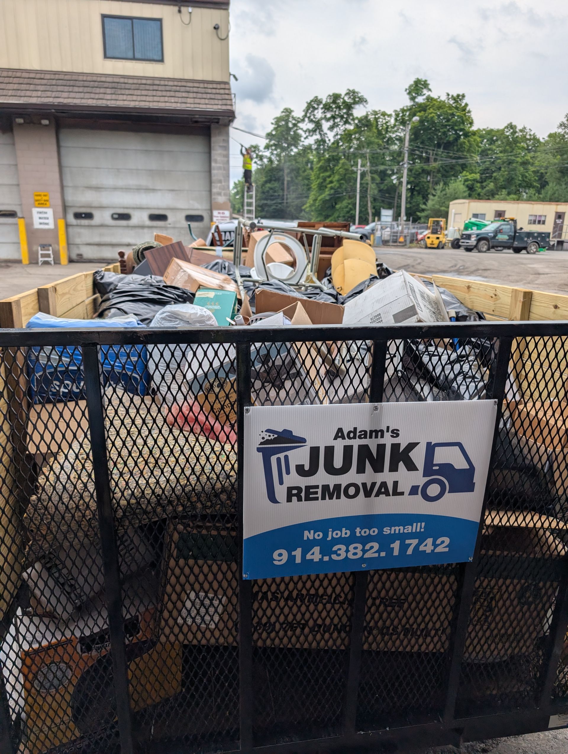 A junk removal dumpster filled with trash, Adam's Junk Removal sign, industrial setting.