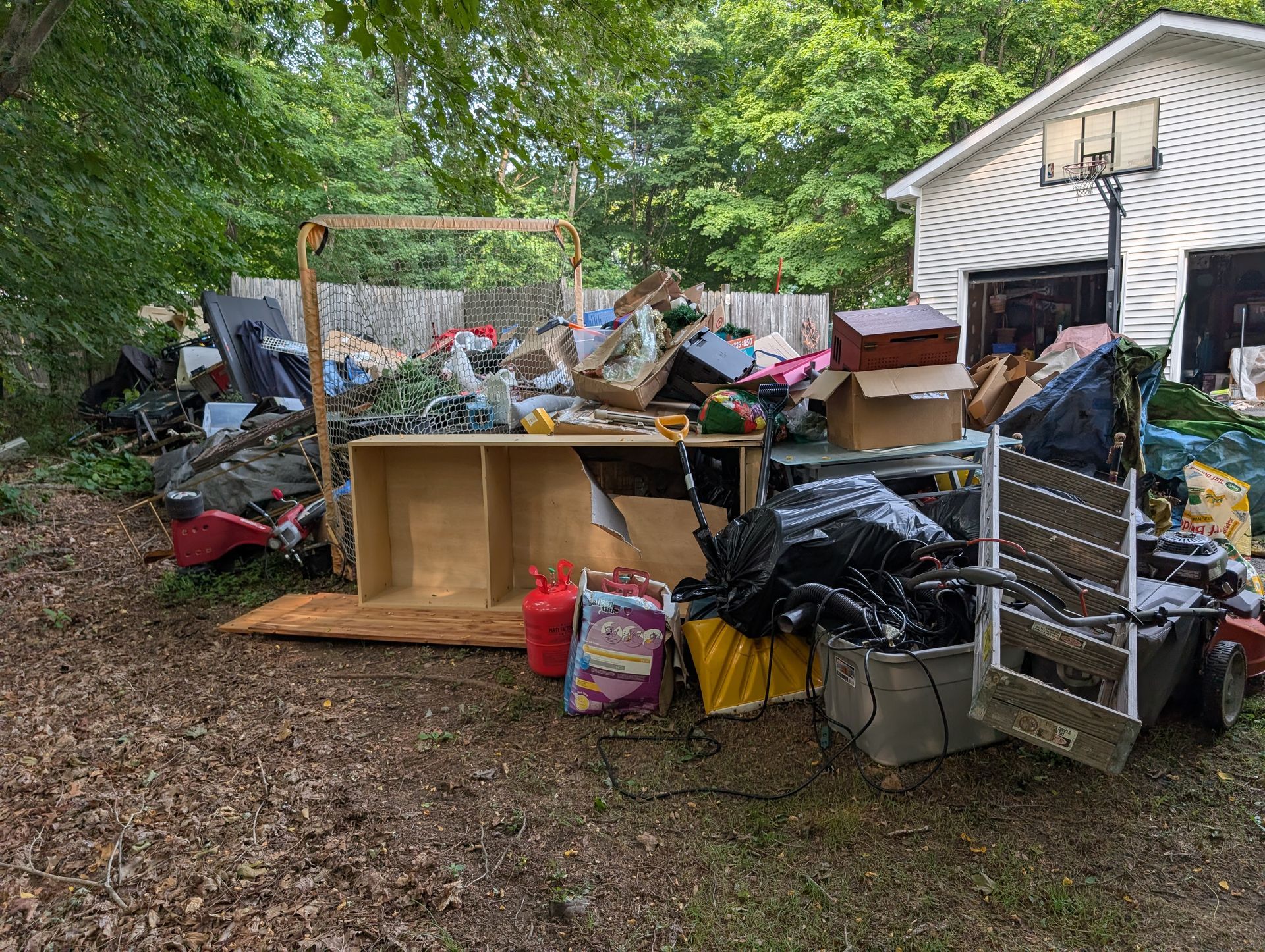 Pile of trash and debris in a yard; includes cardboard boxes, black bags, and furniture.