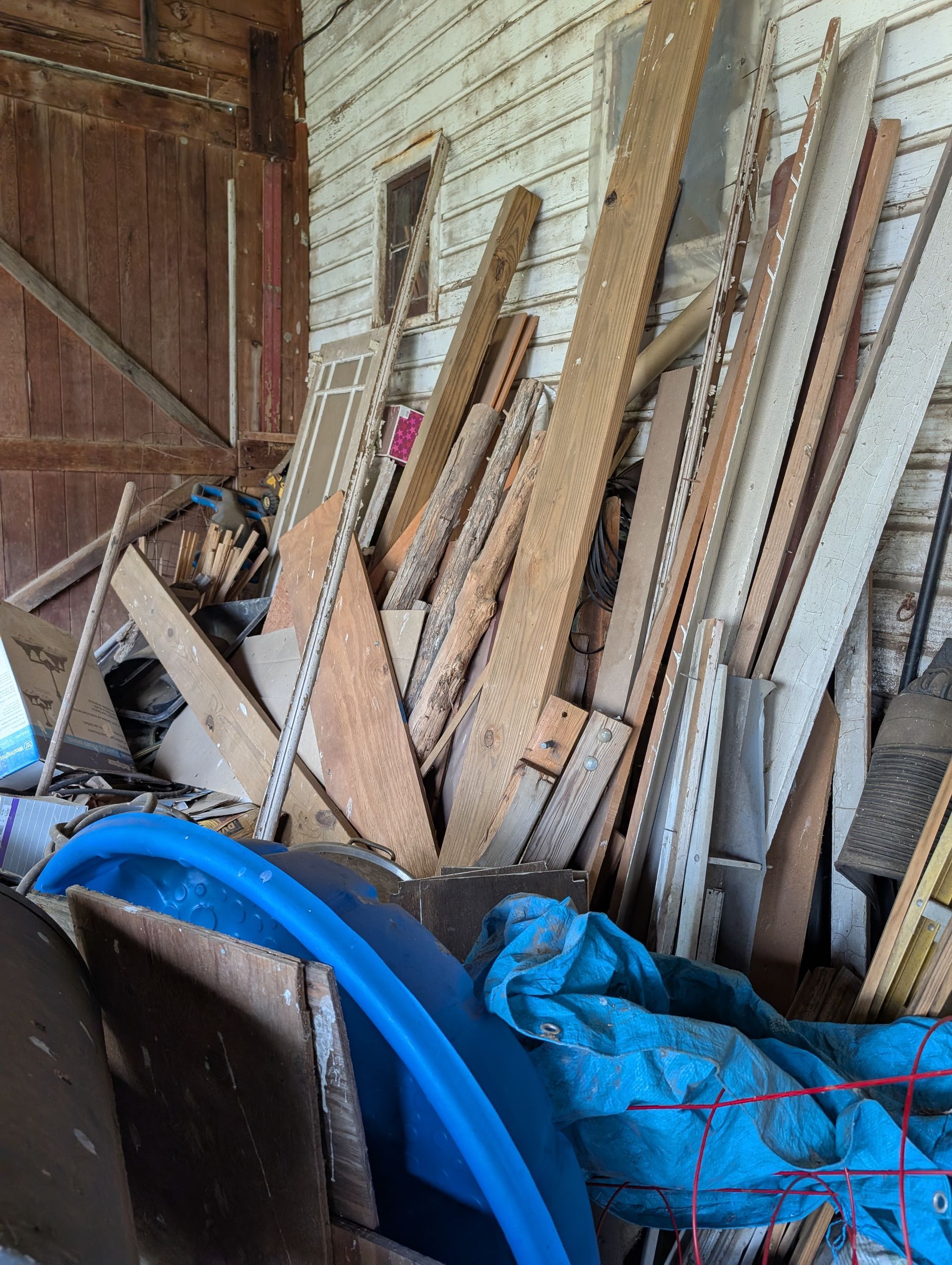 Pile of wood scraps against a weathered, white-planked wall; blue tarp and kiddie pool in the foreground.