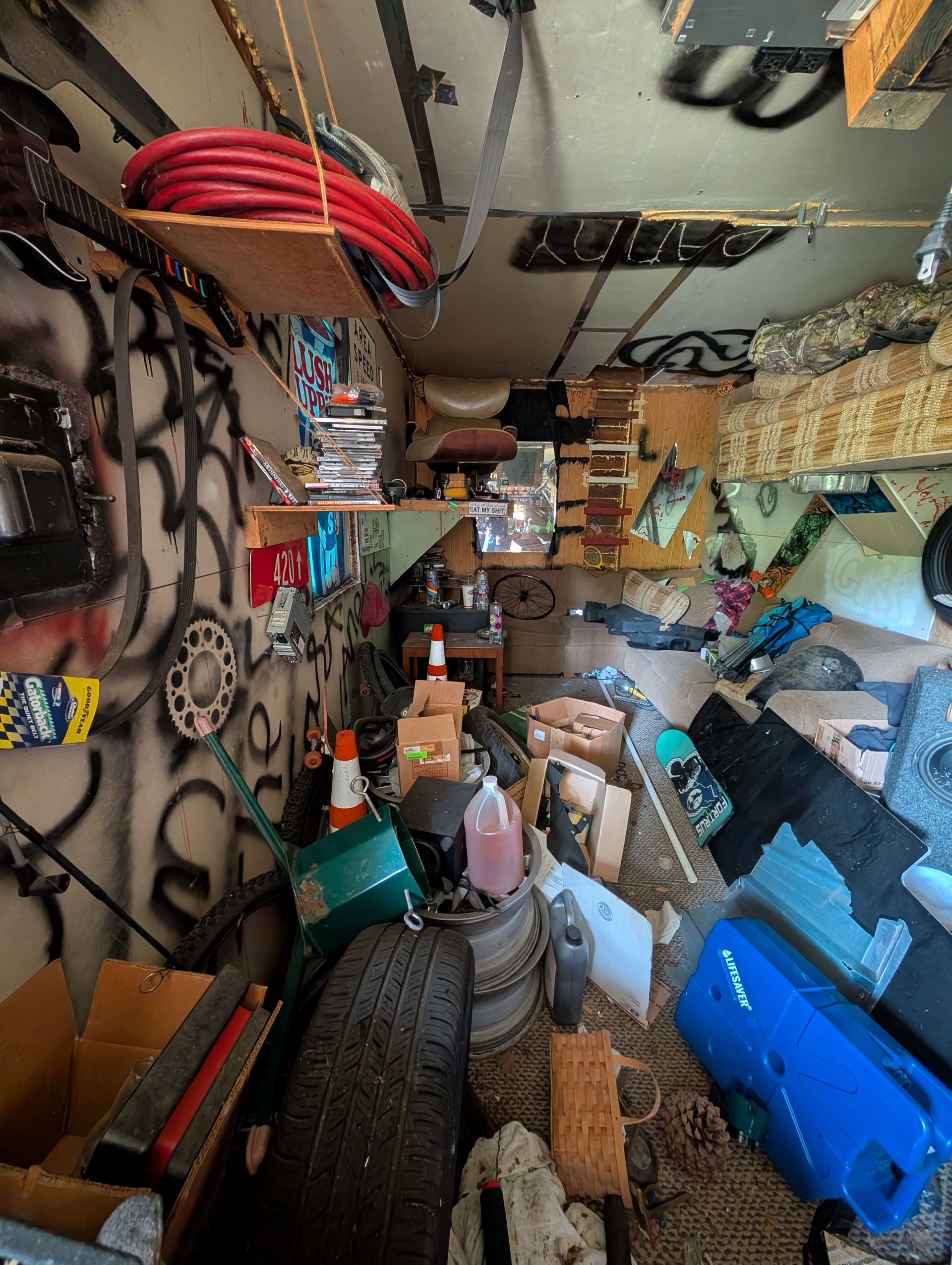 Messy storage area. Graffitied walls, shelves stacked with items, and various objects clutter the floor.