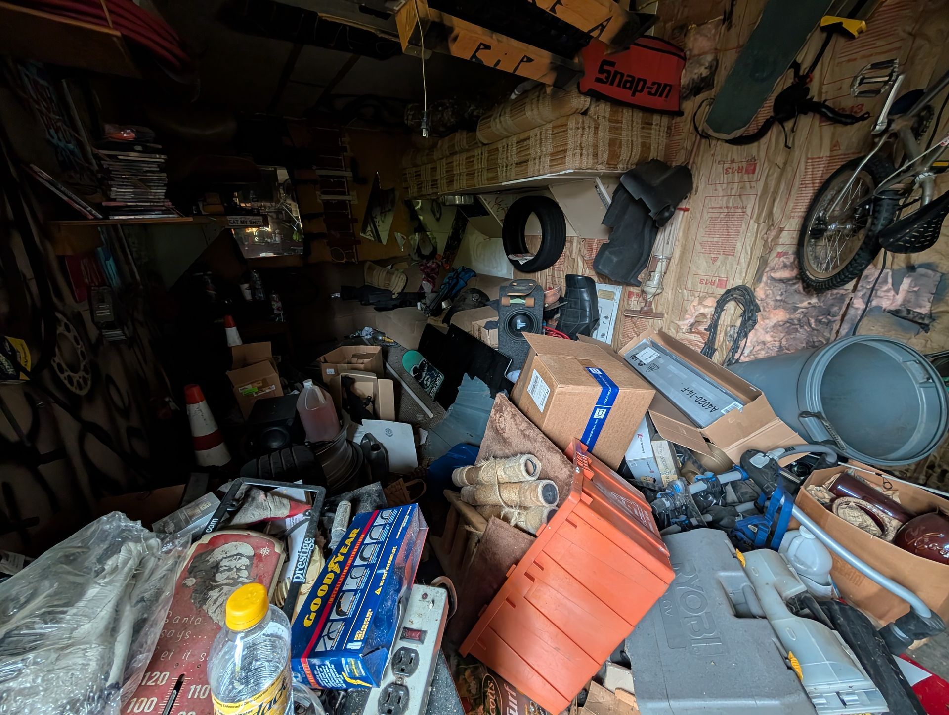 Cluttered shed interior filled with tools, boxes, and various equipment. Dark, poorly lit space.