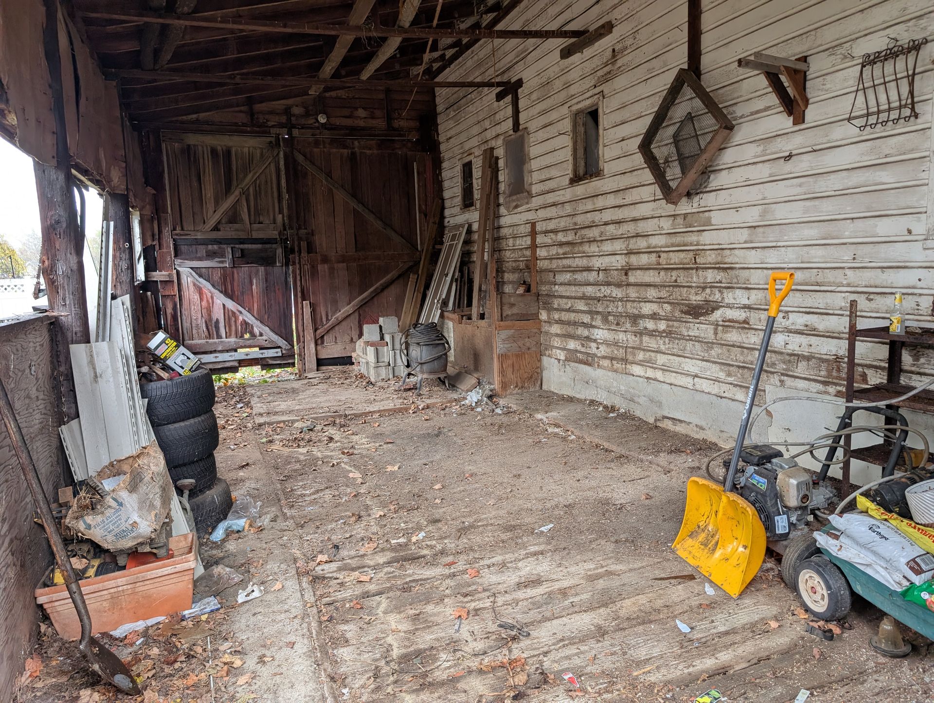 Dilapidated shed interior with debris and tools; dirt floor, weathered wood walls, and open doorway.
