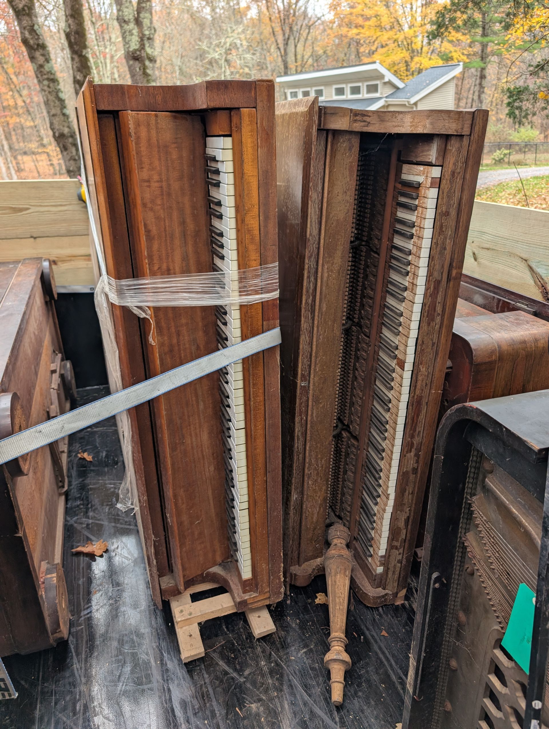 Two antique organs loaded in a truck, leaning against each other. Brown wood, keys visible.