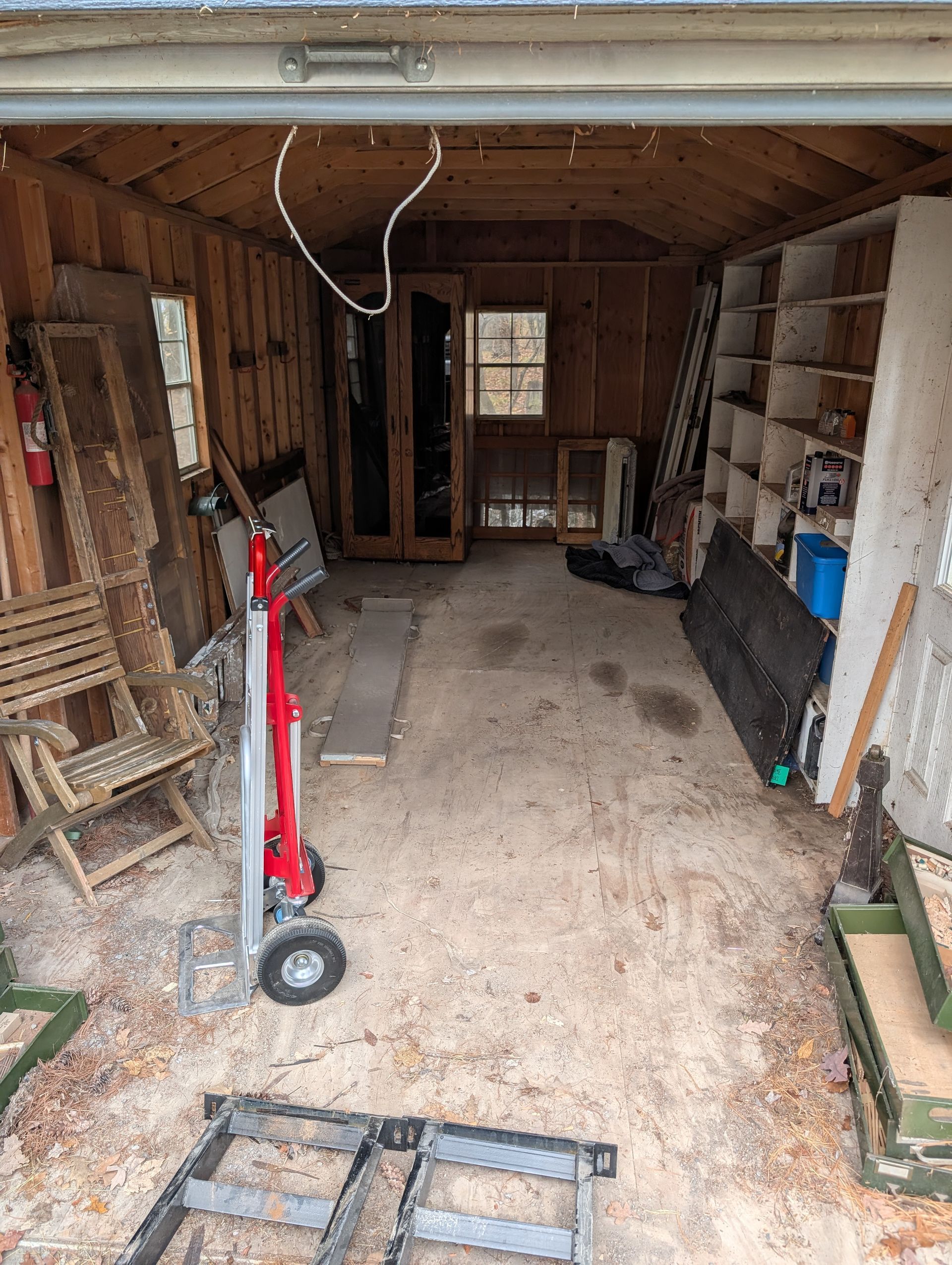 Interior of a dilapidated sunroom with dirt floor, wood walls, and windows overlooking a vehicle.