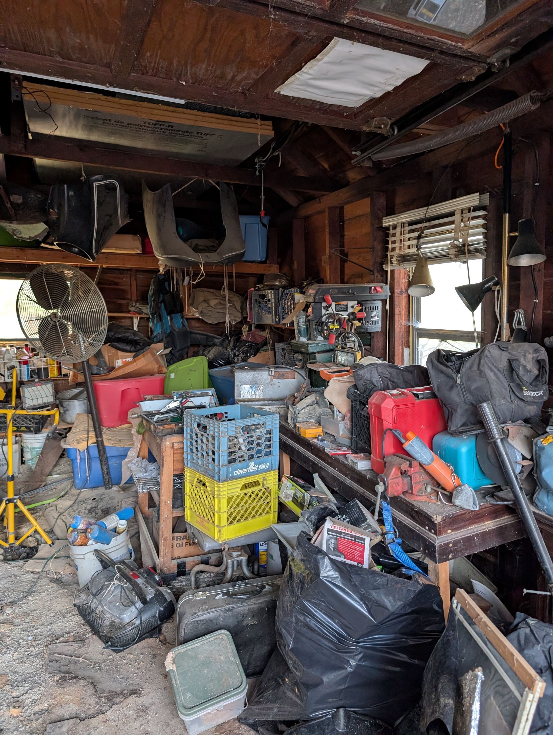 Cluttered garage interior filled with tools, boxes, bags, and miscellaneous items.