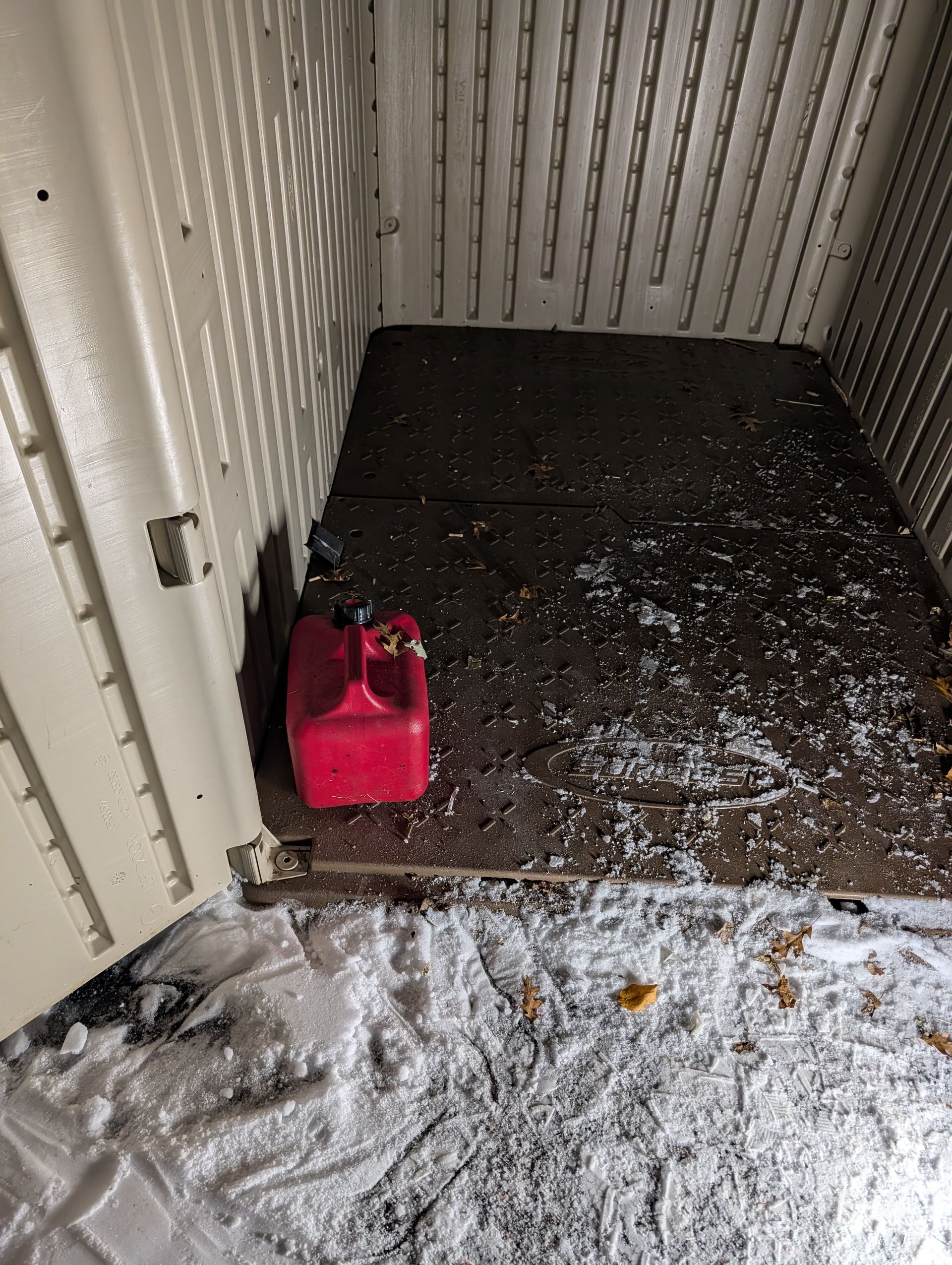 Inside a white shed, a red gas can sits on a dark, snow-covered floor.