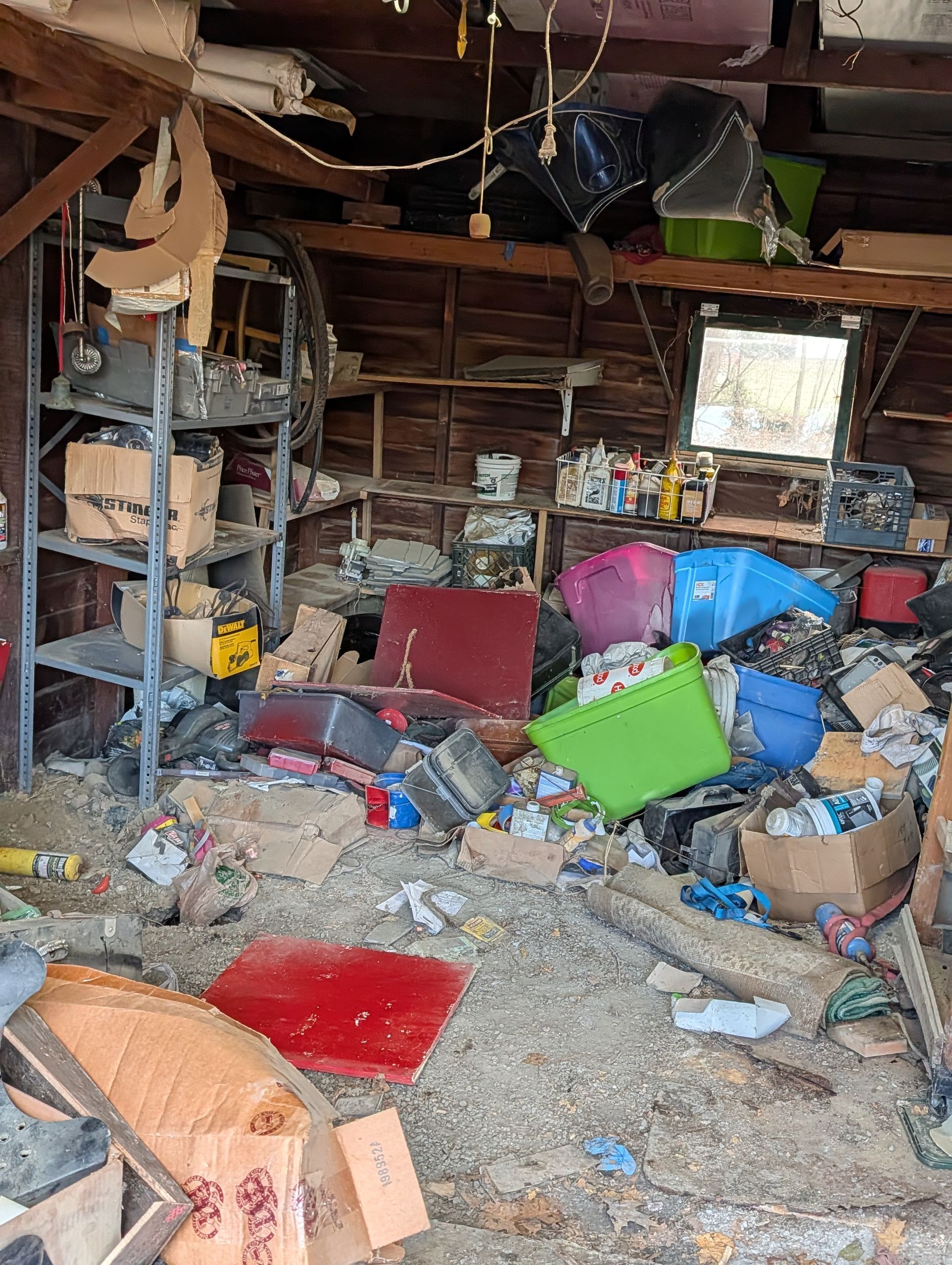 Cluttered, messy garage with shelves, boxes, and various items. Interior shows wooden beams, scattered debris, and storage bins.