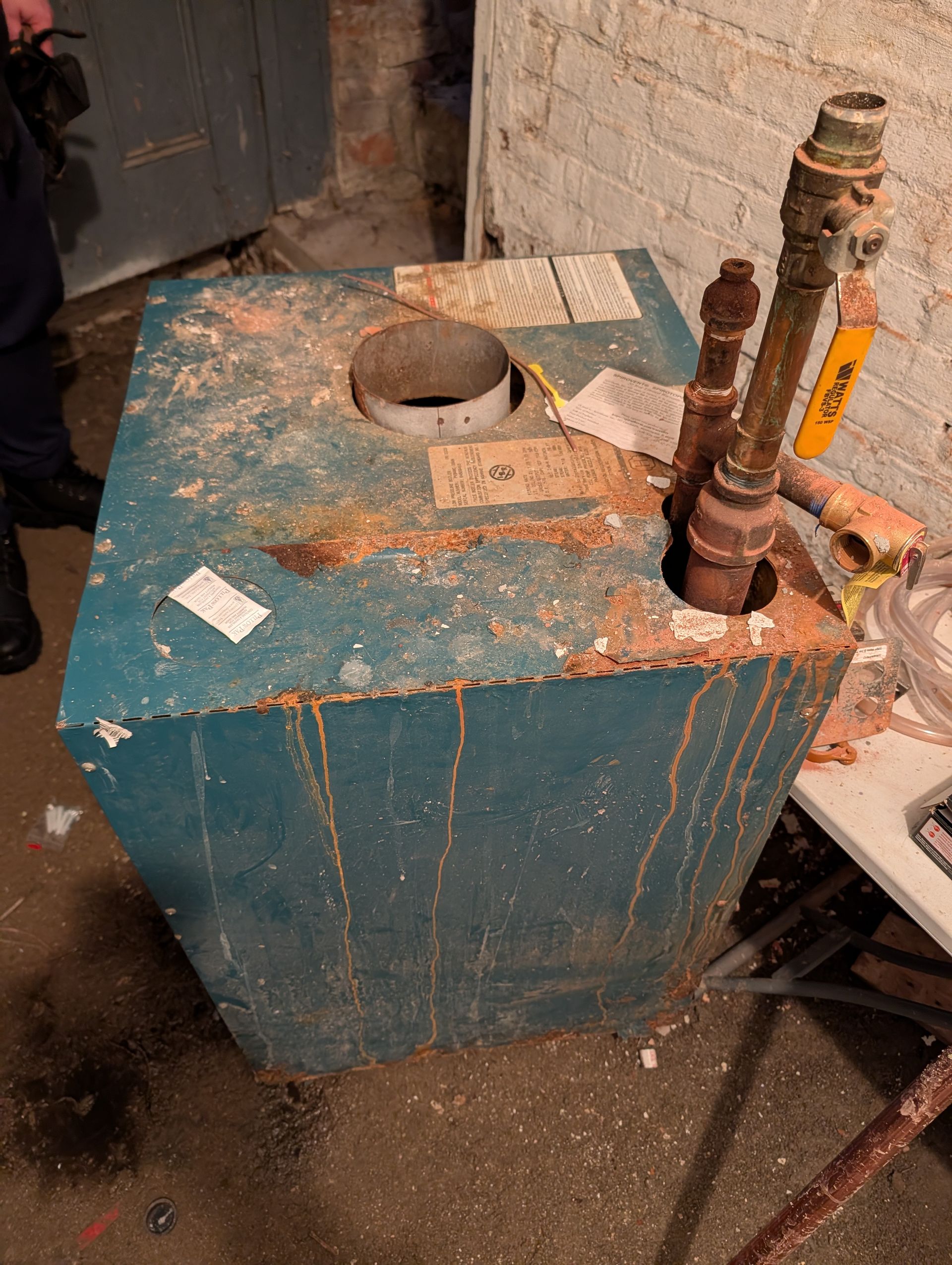 A corroded blue boiler in a basement, with exposed pipes and rust streaks.