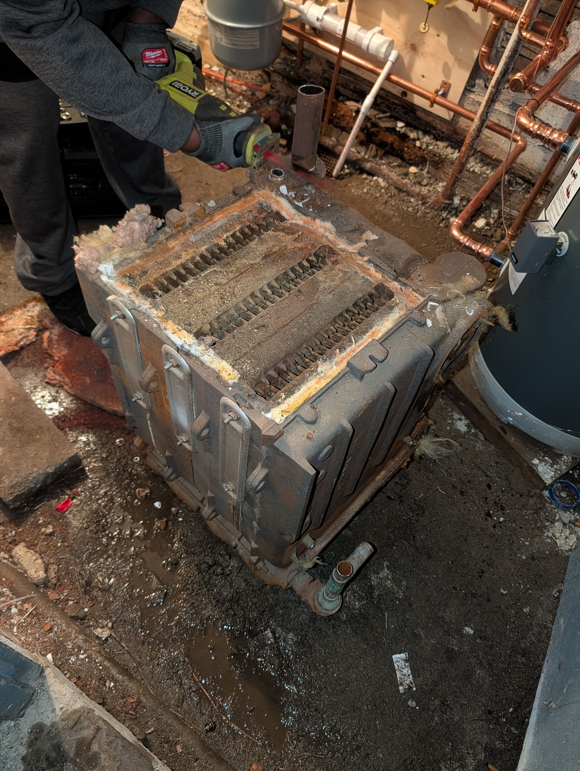 Person working on a rusty boiler in a damp basement; debris scattered around.