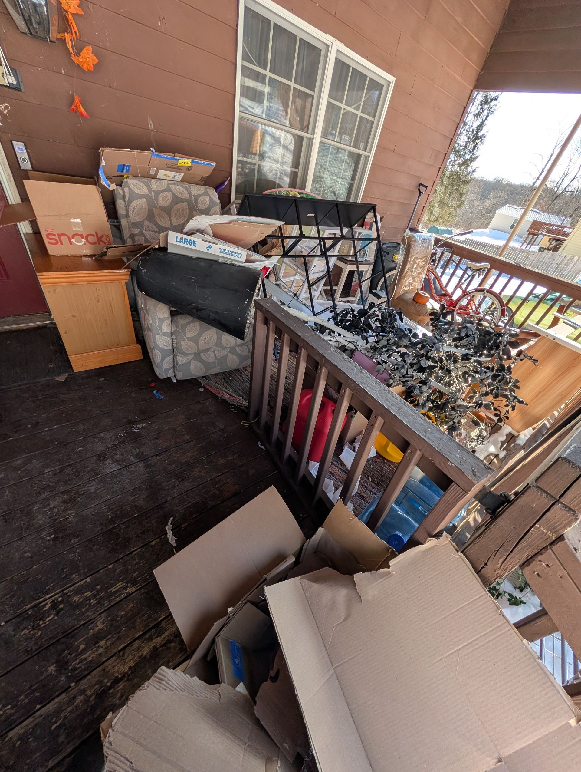 Porch cluttered with cardboard boxes, furniture, and debris near a window and railing. Porch cluttered with cardboard boxes, furniture, and debris near a window and railing.