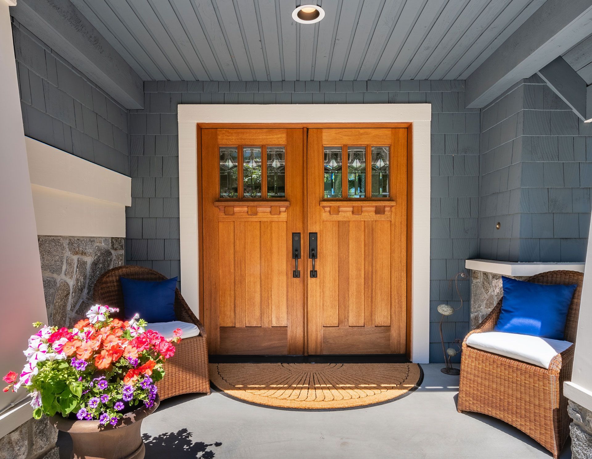 A porch with wicker chairs and flowers in front of a wooden door.