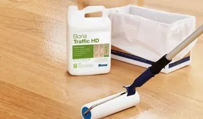 Floor cleaning supplies beside a mop: Bona Traffic HD can and white paint tray on a wooden floor.