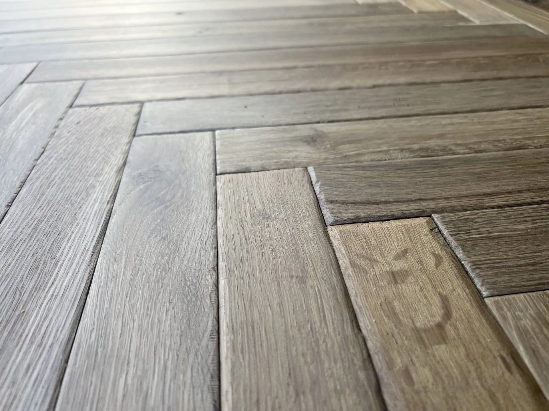 Close-up of light gray and tan wooden floor planks in a herringbone pattern