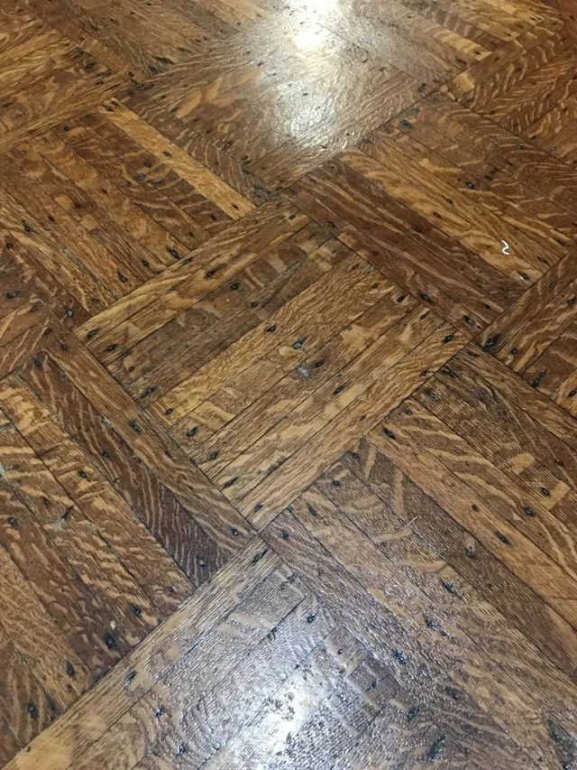 Close-up of worn brown parquet wood flooring with a glossy reflective patch.