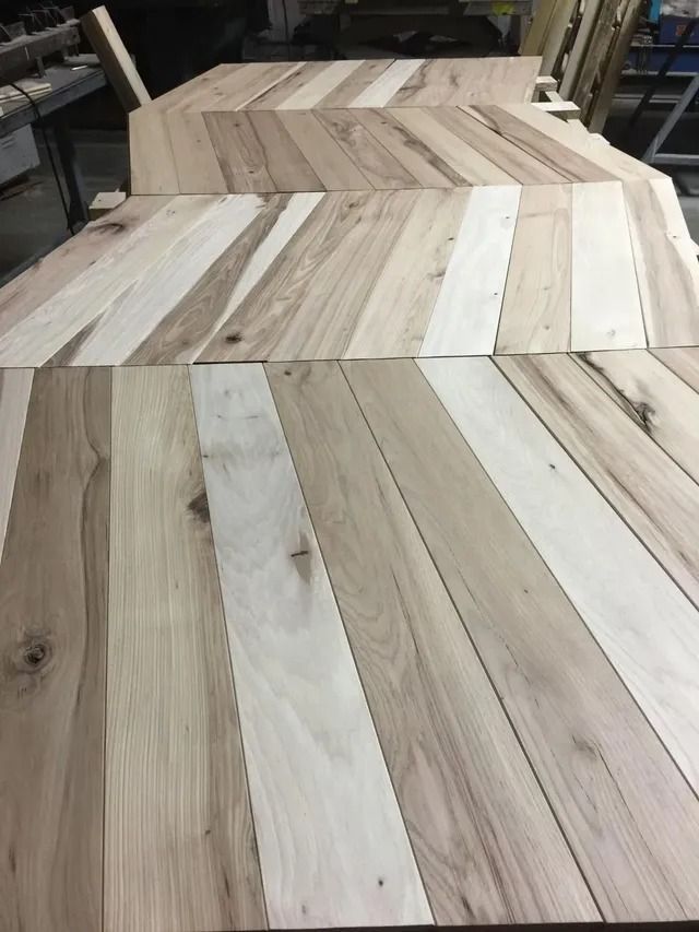 Stacked wooden herringbone tabletop panels in a workshop, showing light and dark wood strips.