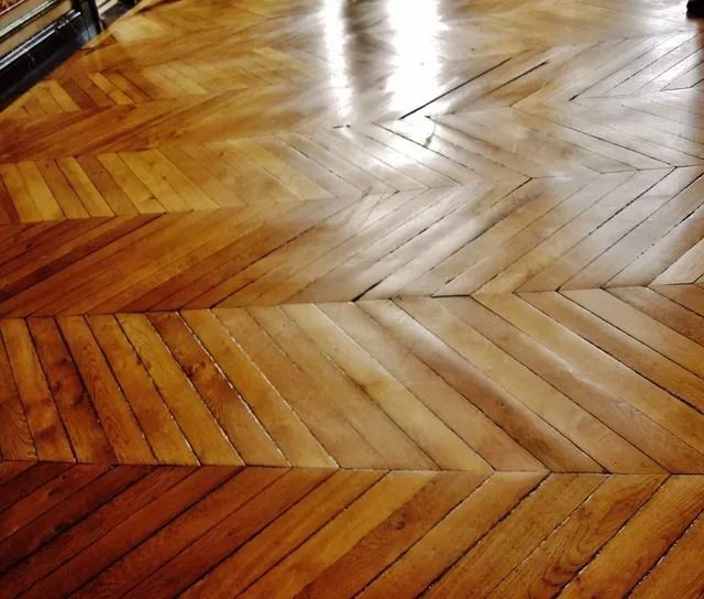 Polished wooden parquet floor with herringbone pattern and a bright sunlit reflection