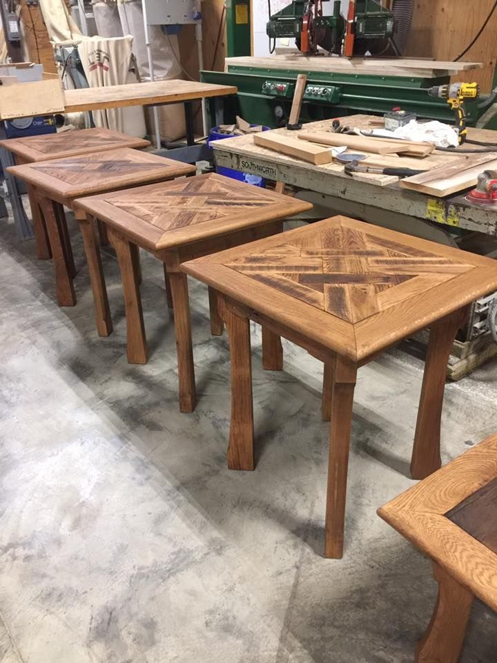 Four wooden square stools with patterned tops in a workshop, lined up on a concrete floor.