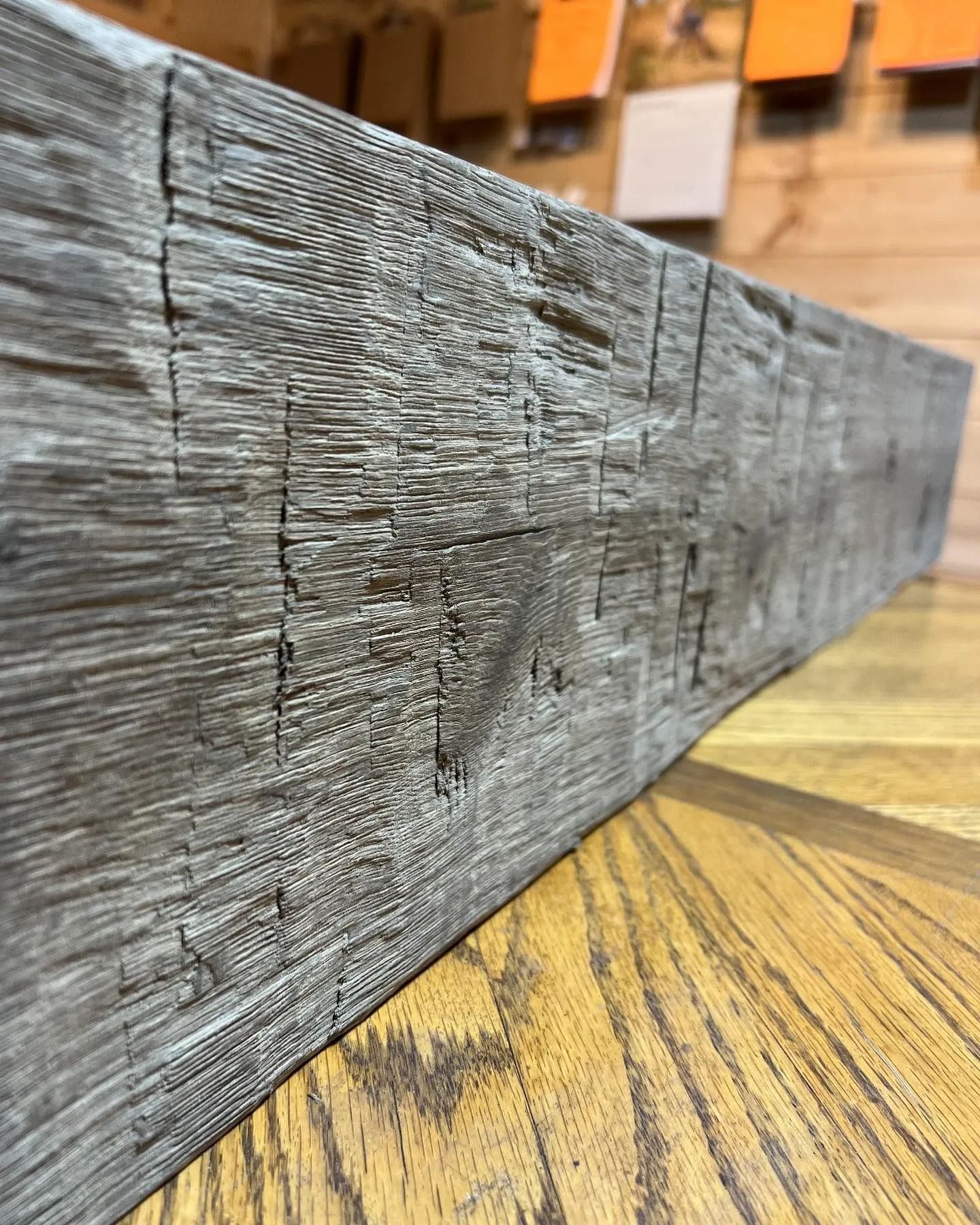 Close-up of a gray weathered wooden beam on a patterned wood floor.