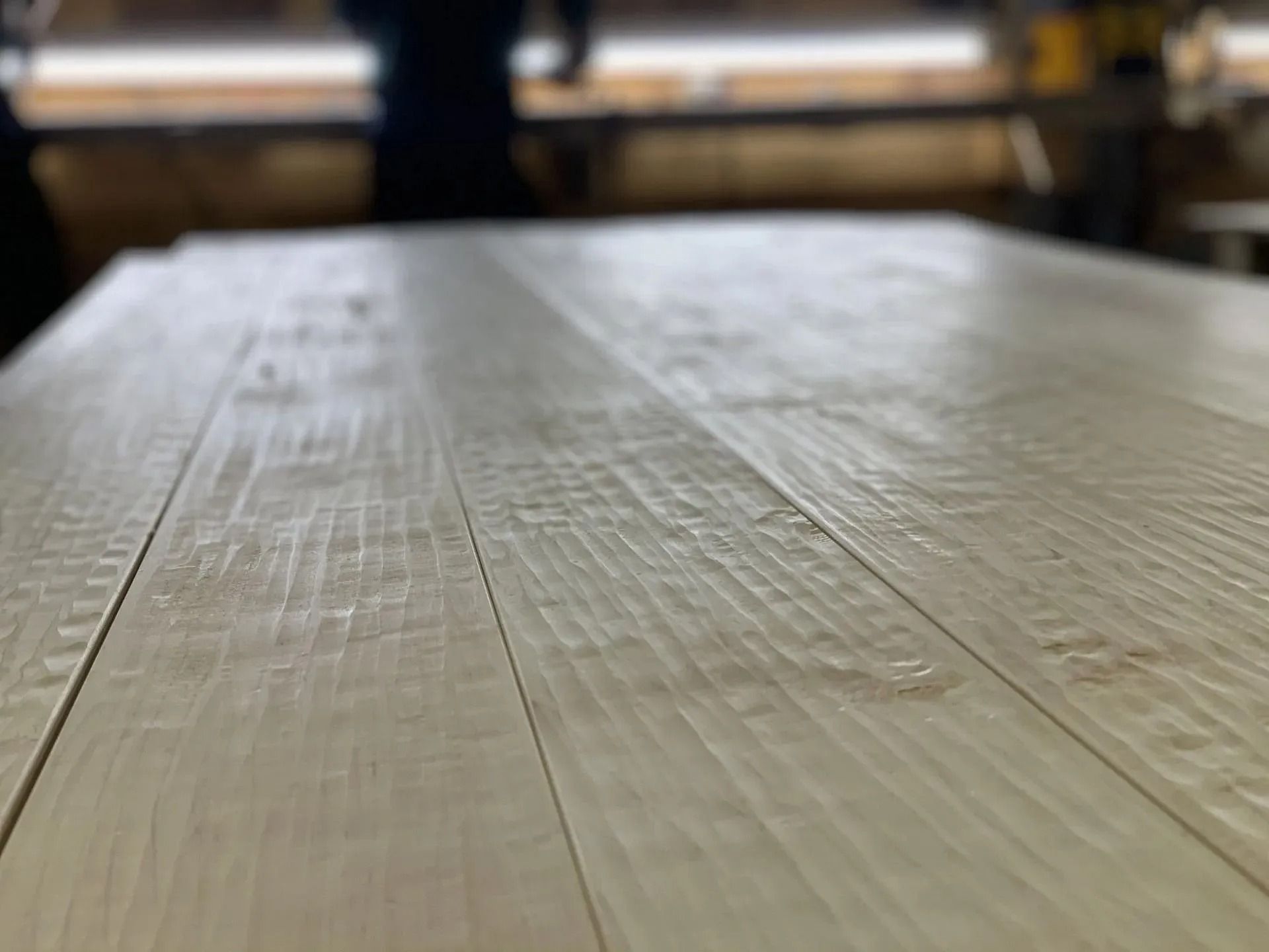 Close-up of a light wooden tabletop with blurred chairs in the background.