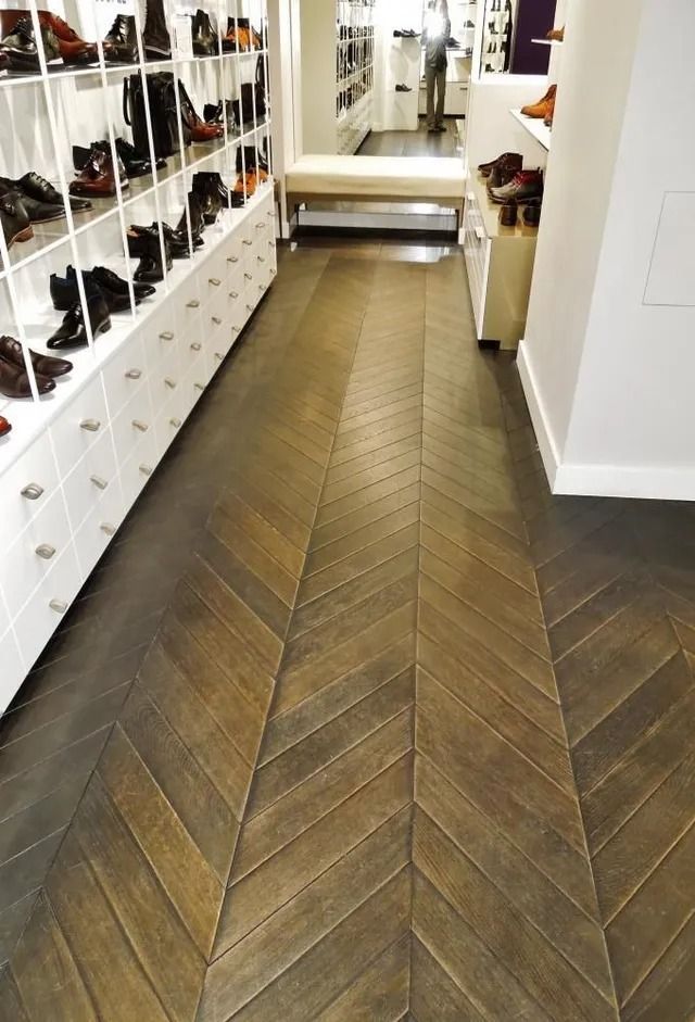 Shoe store aisle with herringbone wood floor, white shelving, and a mirror at the end.