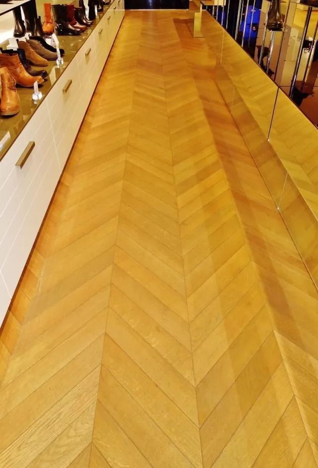 Wooden herringbone-pattern floor in a hallway or store aisle, with shelves along both sides