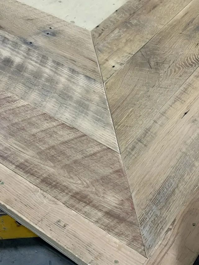 Close-up of a light wood tabletop with herringbone grain pattern and a beveled corner.