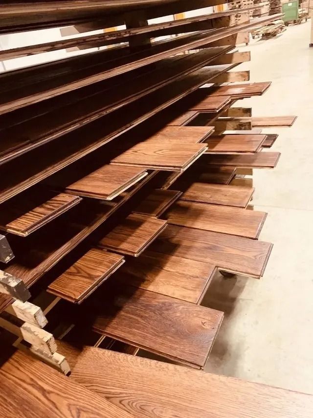 Stacks of wooden shelves and boards in a workshop aisle, showing various brown wood planks