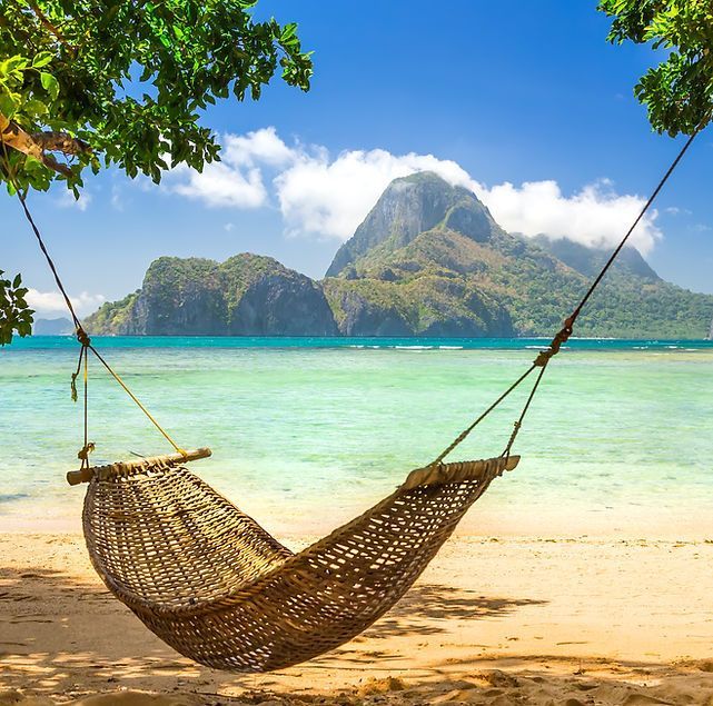 Hammock on a tropical beach with turquoise water and mountain backdrop.