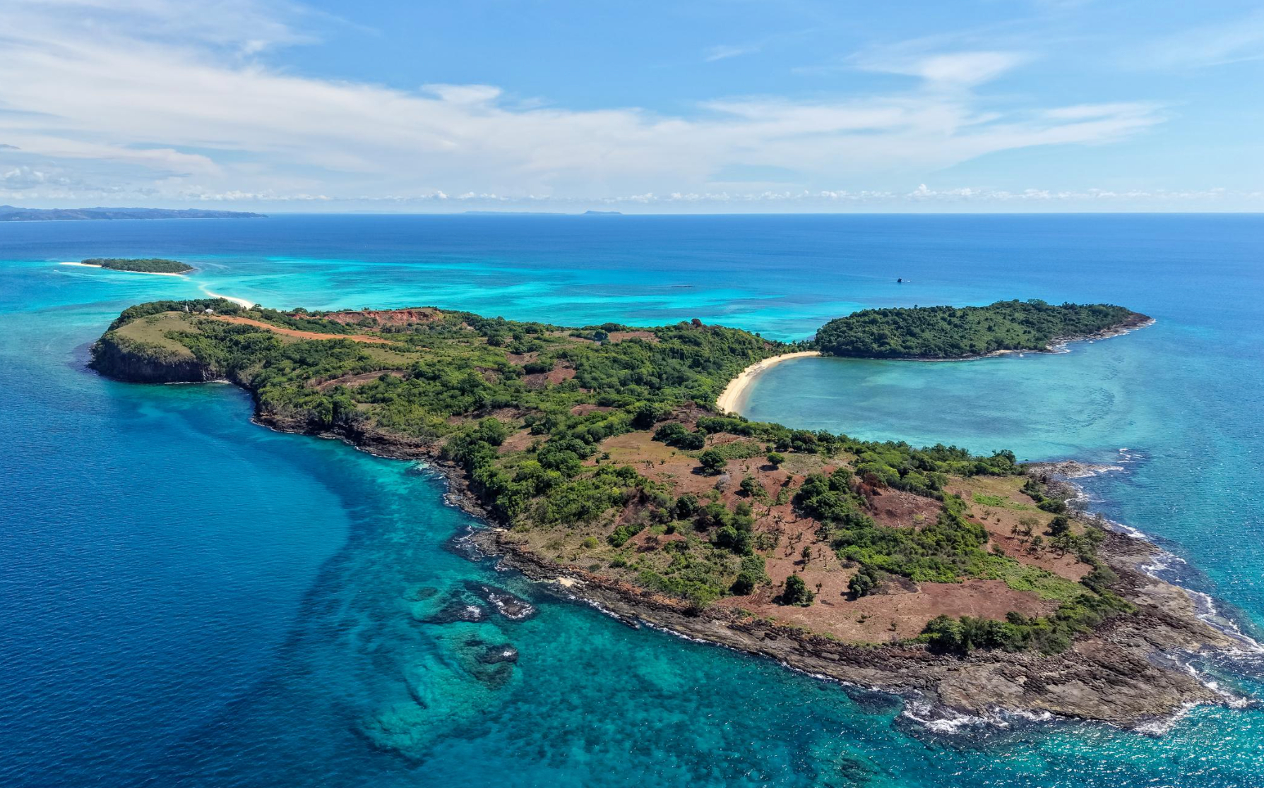 Island with lush green vegetation surrounded by turquoise ocean, clear skies.