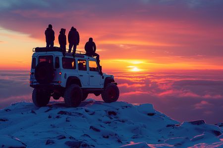 People on top of a white off-road vehicle watch a vibrant sunset from a snow-covered peak.