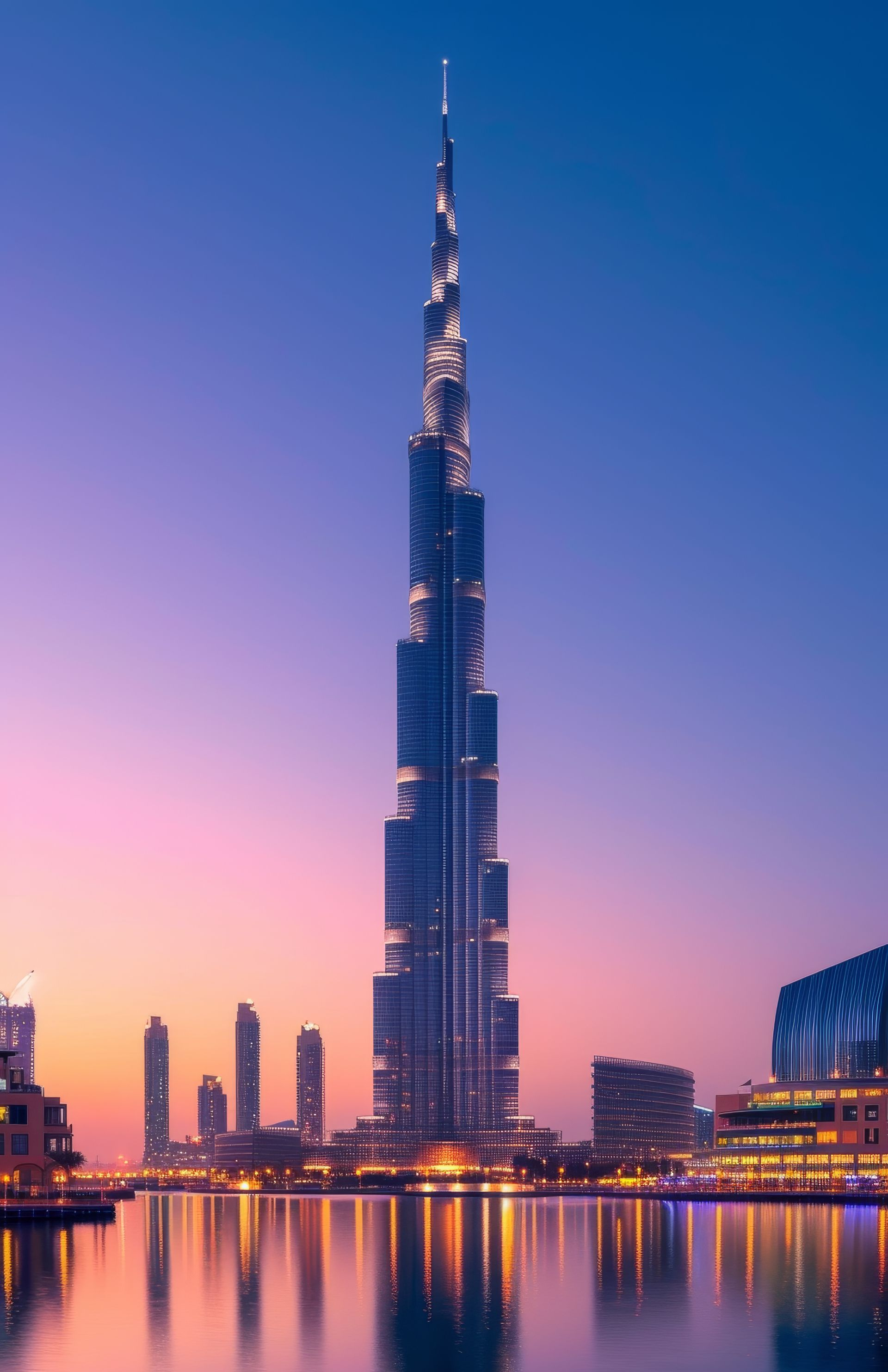 Burj Khalifa skyscraper at dusk reflecting in water, Dubai. Pink and purple sky with city lights.