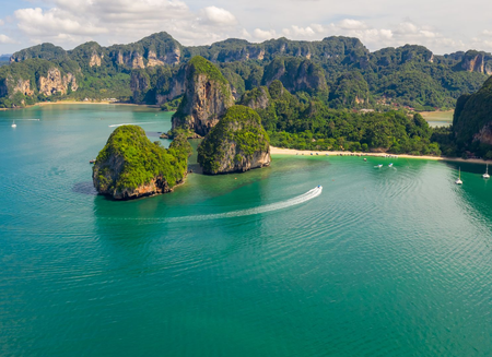 Turquoise ocean with limestone cliffs and lush green islands; a boat leaves a white wake.