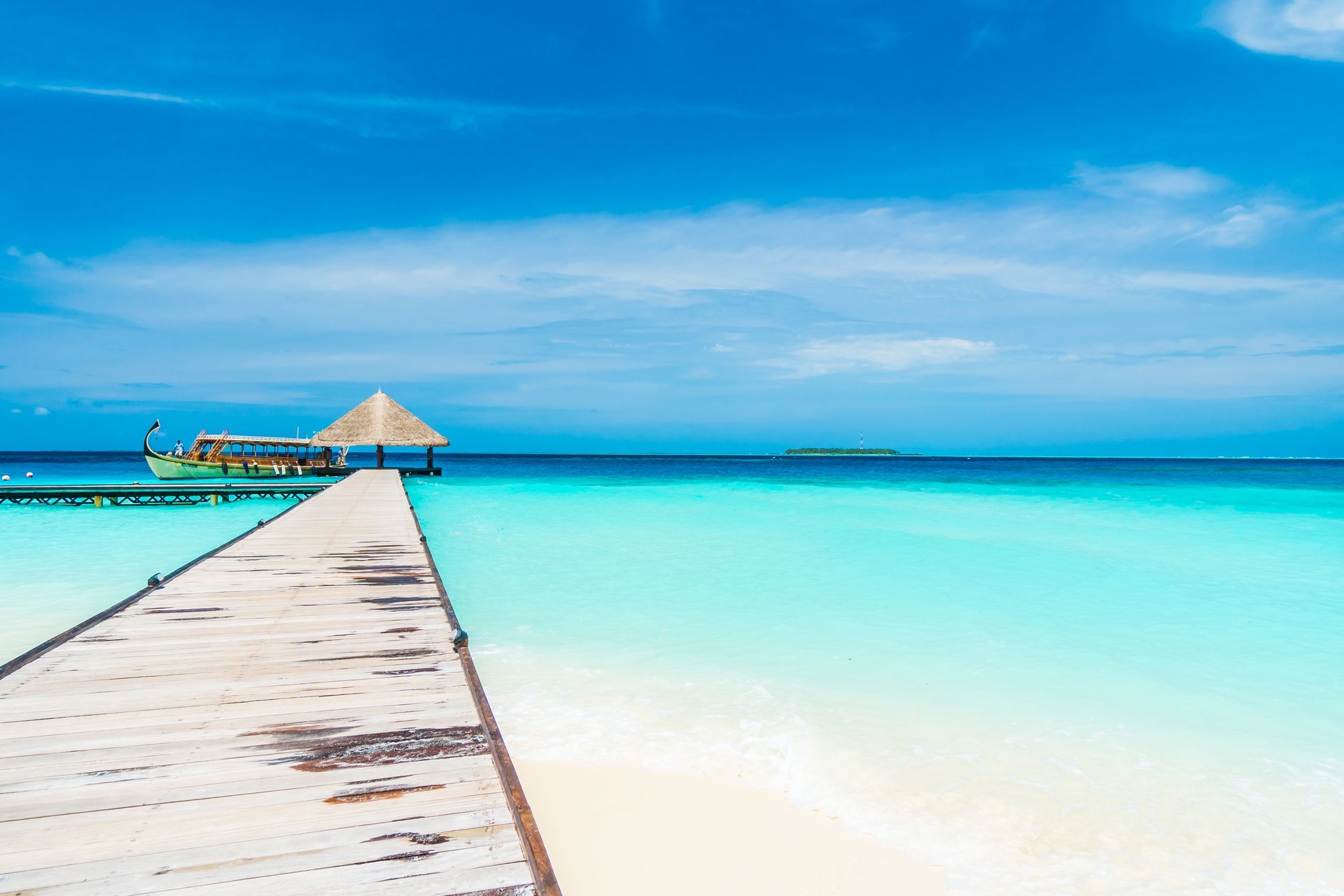 Wooden pier extending into turquoise ocean with clear blue sky and a small boat.