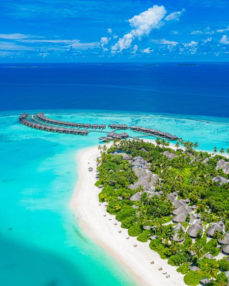 Aerial view: Tropical island with white sand, turquoise water, and overwater bungalows.