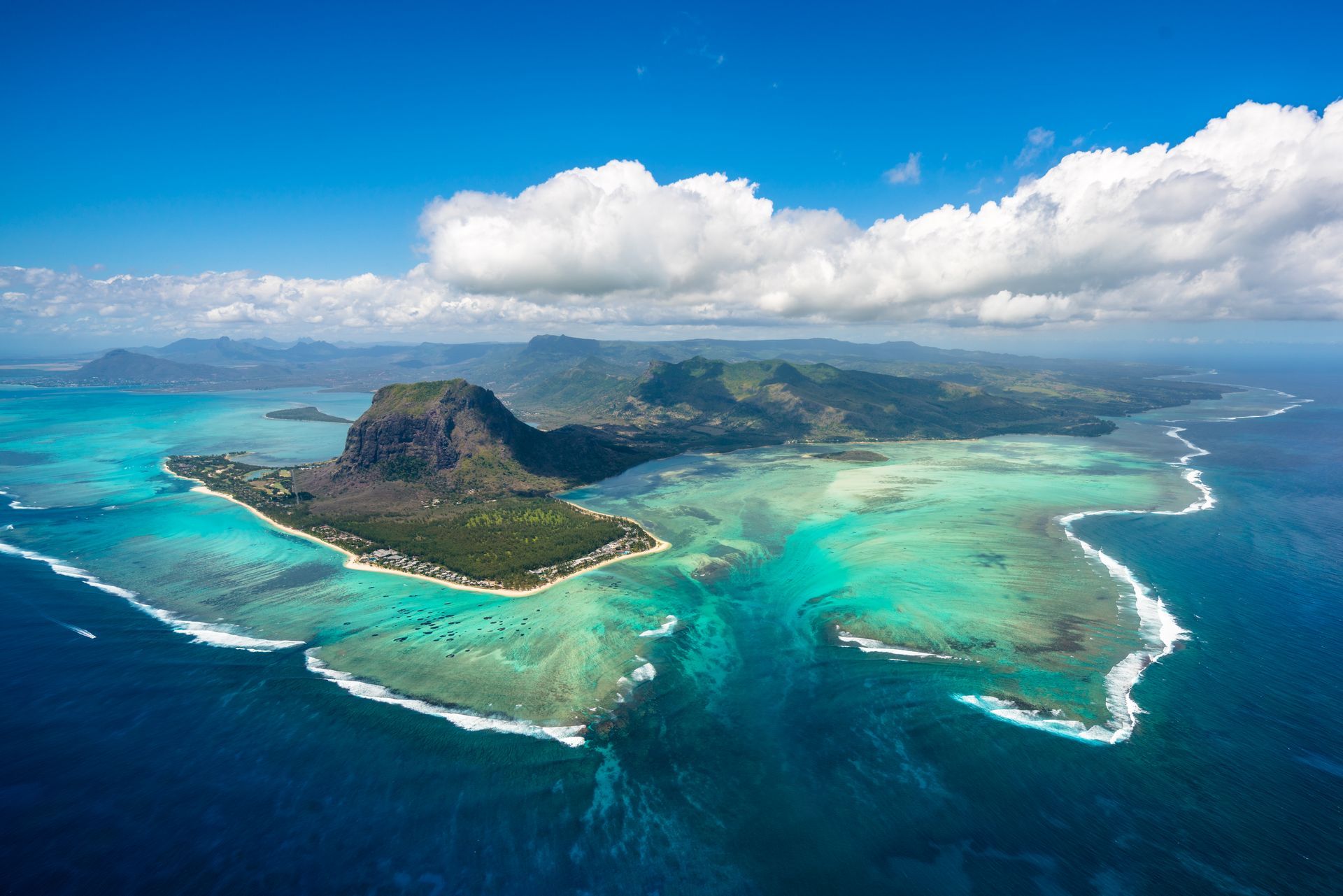Aerial view of Mauritius island, turquoise water, white sand, lush green vegetation, and blue sky.