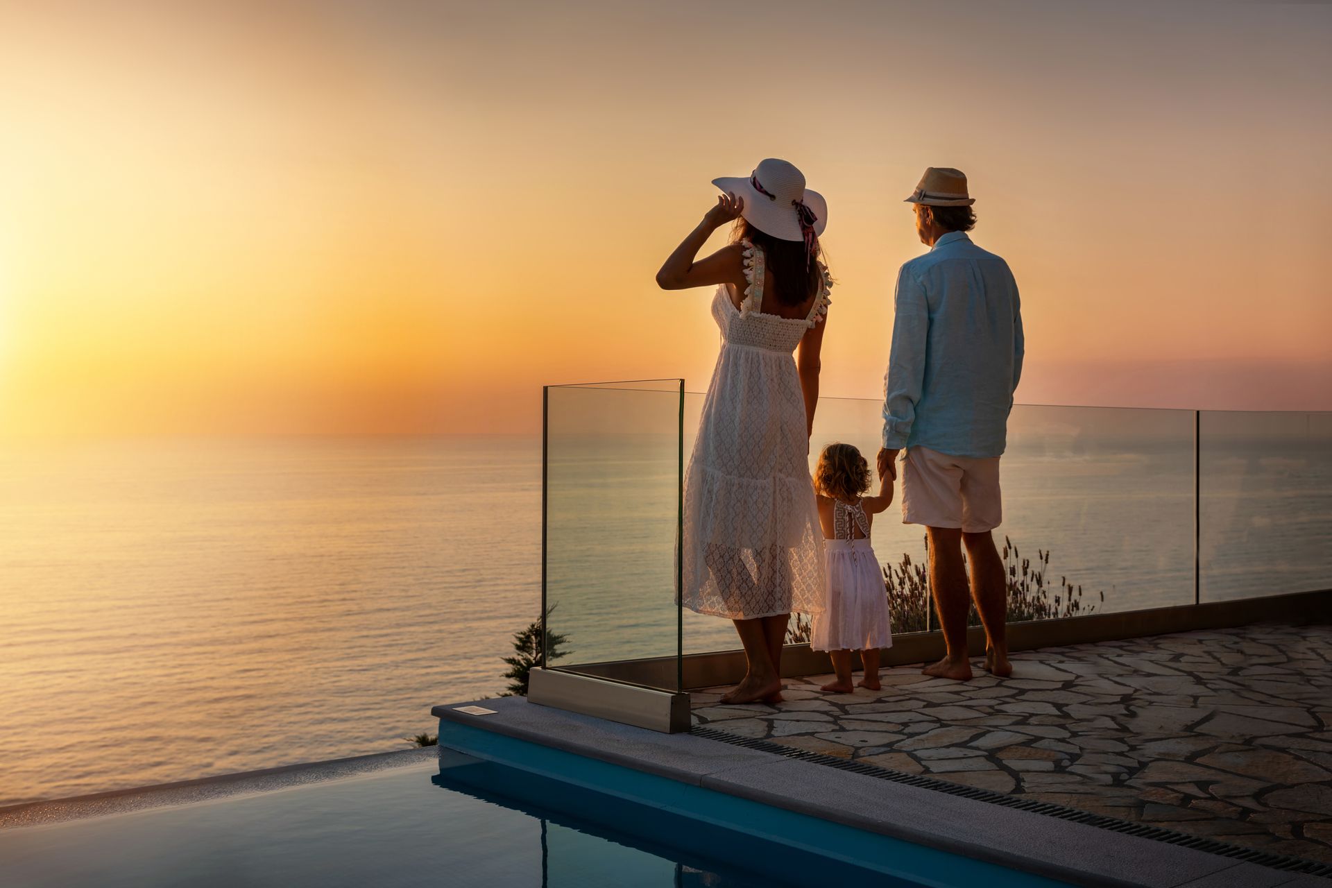 Family watching sunset over ocean from a patio with a pool.