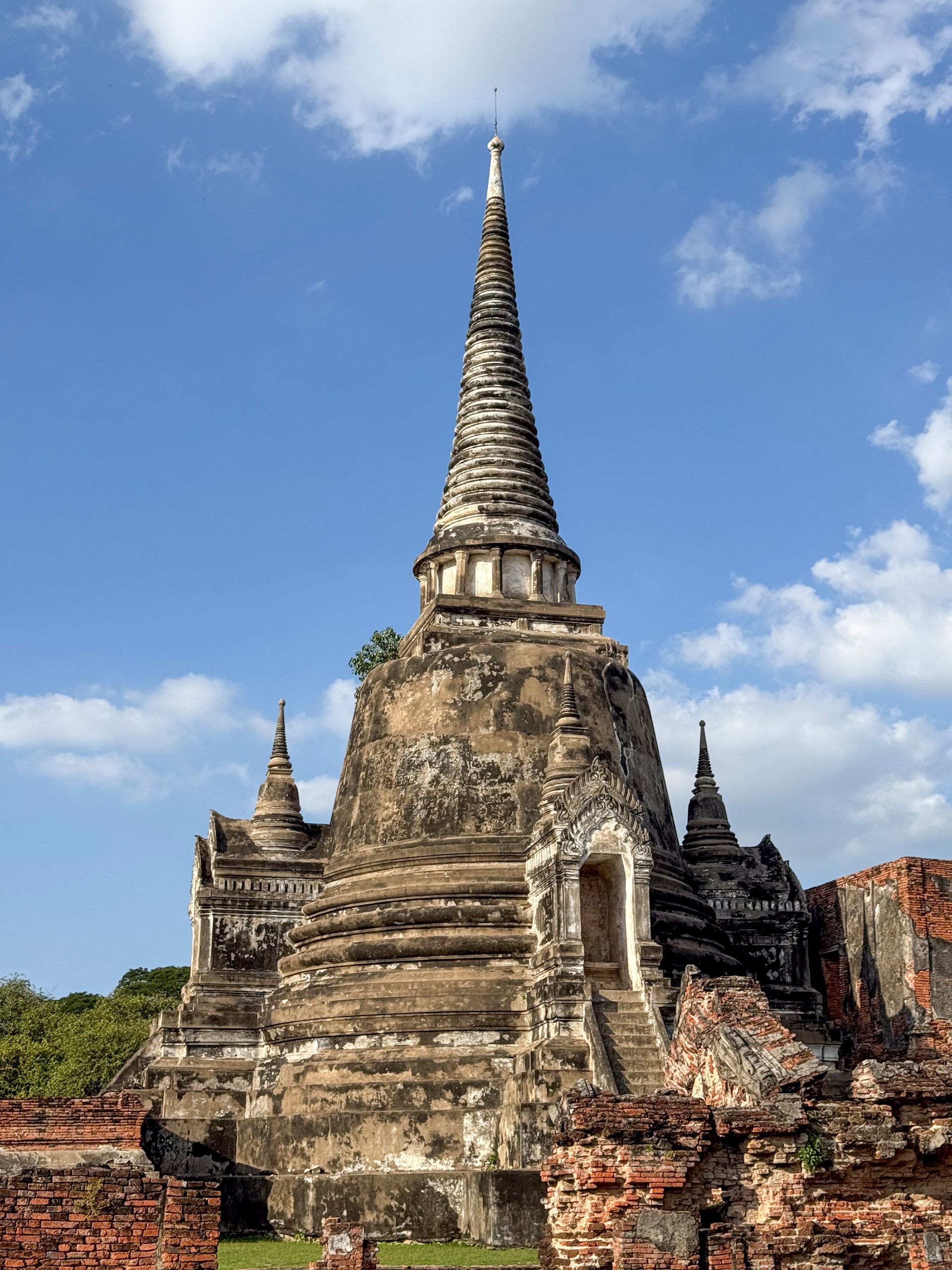 Ancient, weathered stupa with a tall, conical spire against a blue sky.