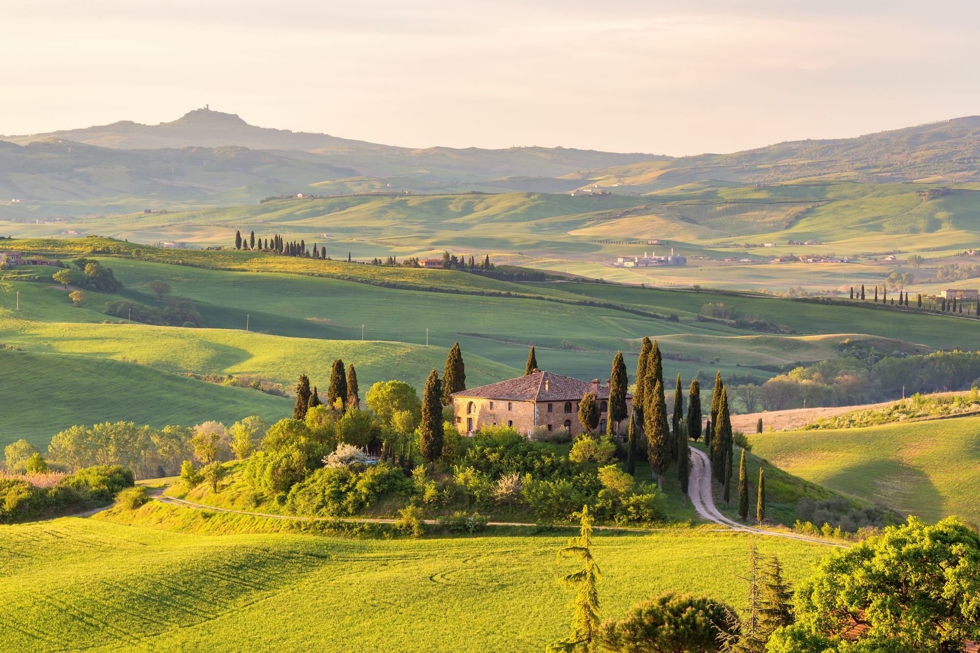 Rolling green hills of Tuscany with a villa and cypress trees under a soft, golden light.