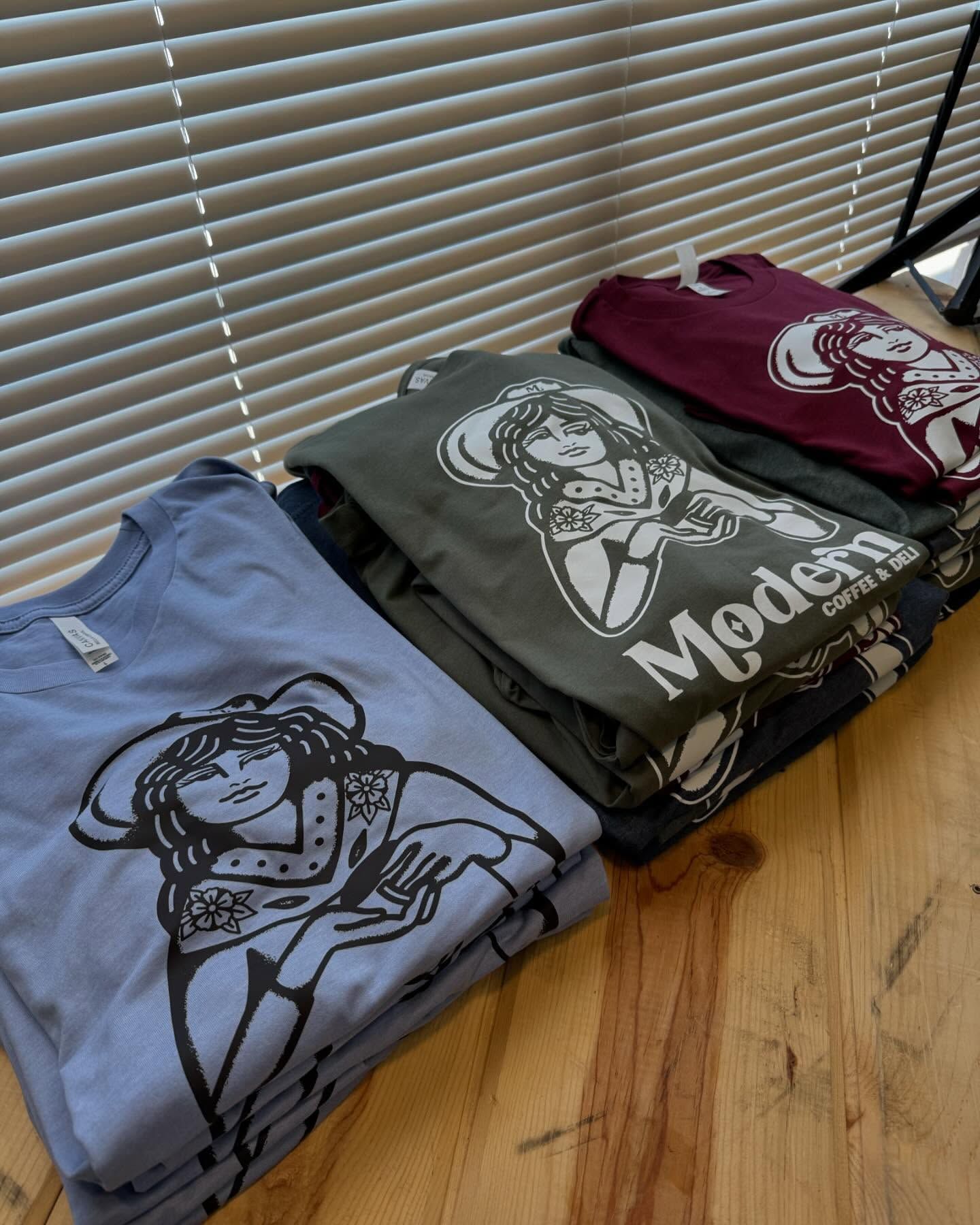 Stack of modern cowgirl t-shirts in blue, green, and burgundy, with matching graphic print.