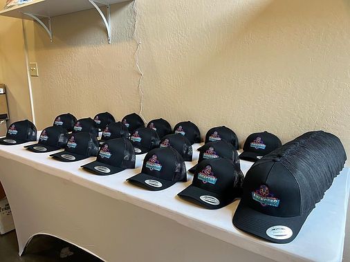 A table with many black baseball caps, each with a logo, displayed indoors.