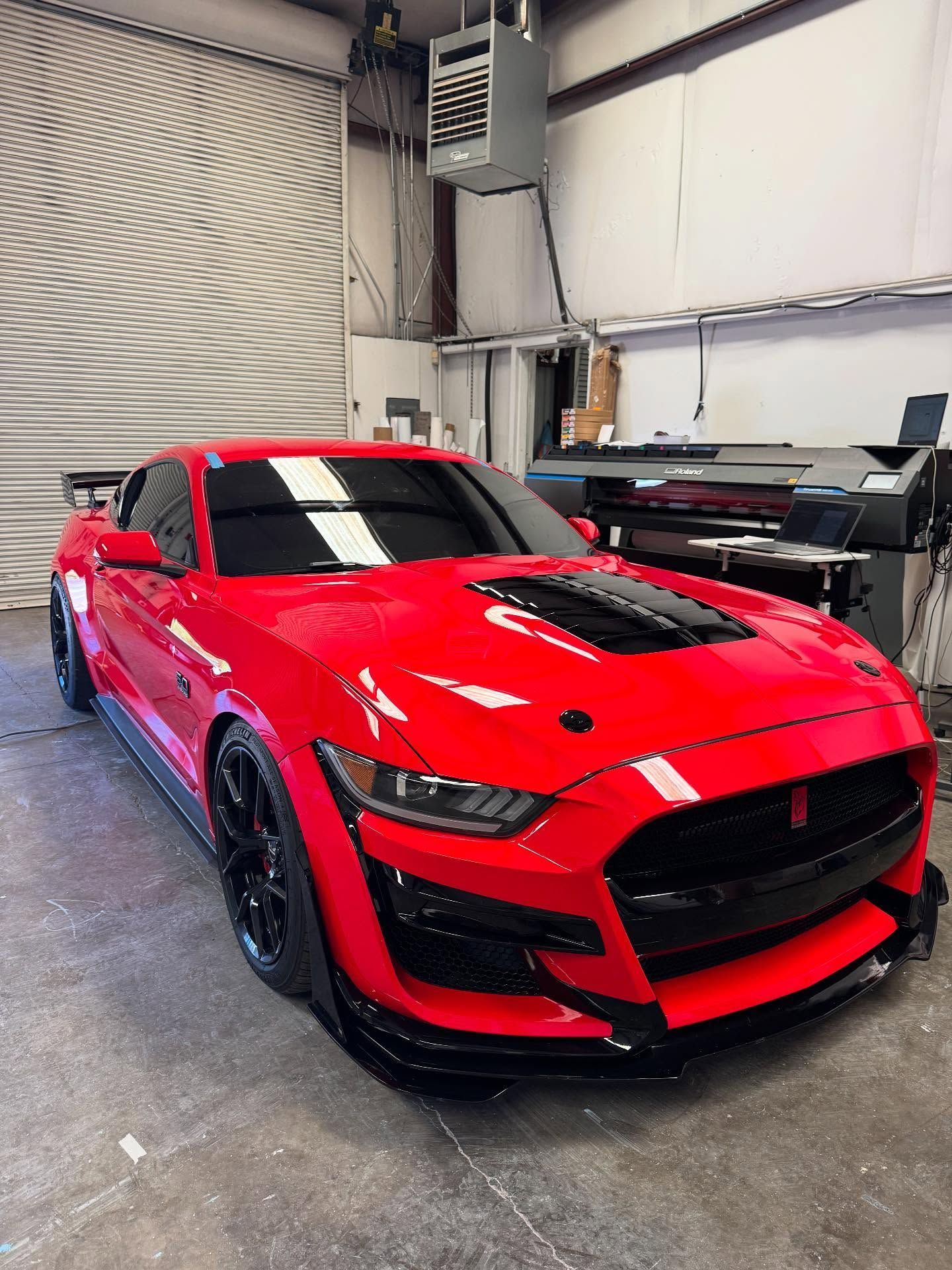 Red Ford Mustang Shelby GT500 sports car with black accents parked inside a garage.