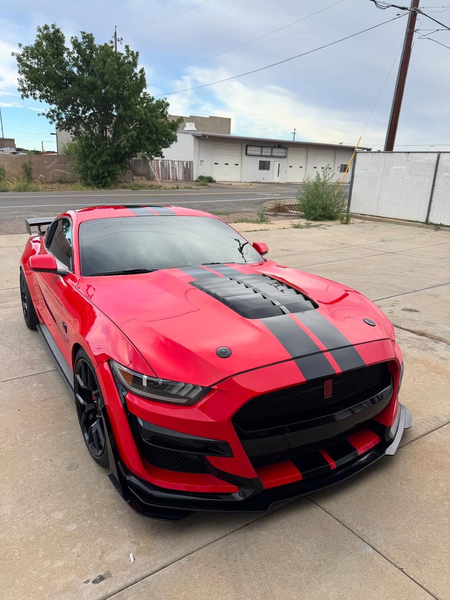 Red Ford Mustang Shelby GT500 with black racing stripes and accents, parked outdoors.